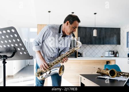Musicien jouant du saxophone dans la cuisine à table à la maison Banque D'Images