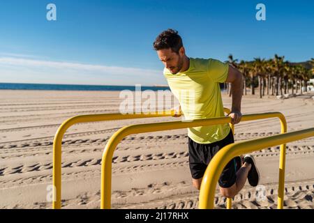 Athlète qui fait des pompes sur des barres parallèles à la plage Banque D'Images