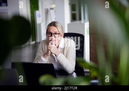 Femme d'affaires attentionnés avec les mains sur le menton regardant un ordinateur portable dans le bureau Banque D'Images