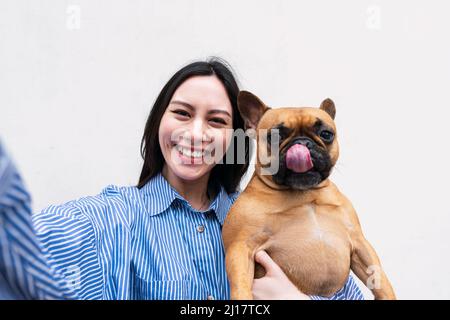 Bonne femme transportant un chien qui colle à la langue devant le mur Banque D'Images