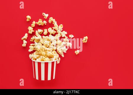 Boîte ronde à rayures avec pop-corn sur fond rouge vif. Vue de dessus, espace de copie pour le texte Banque D'Images