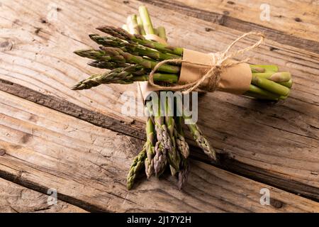 Vue en grand angle des petits pains d'asperges verts crus attachés avec des cordes sur une table en bois Banque D'Images