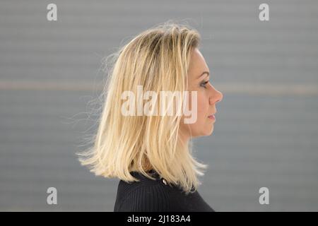 Portrait de profil d'une femme d'âge moyen avec de longs cheveux blonds de longueur d'épaule contre un mur gris Banque D'Images