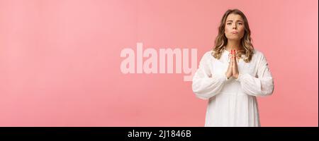 Portrait d'une petite amie pleine d'espoir, blonde fille mendiant pour la faveur en robe blanche sur fond rose, sobbing faire des yeux mignons, pleurer ou prier Banque D'Images