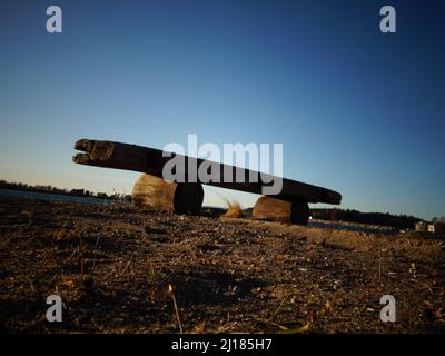 Un banc de bois naturel situé sur une plage de sable presque silhoueté contre le ciel bleu. Banc primitif composé de deux billes et d'un morceau de bois de flotté. Banque D'Images