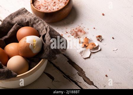 Vue en grand angle des œufs frais cuits dans un bol avec du sel de roche sur une table blanche Banque D'Images