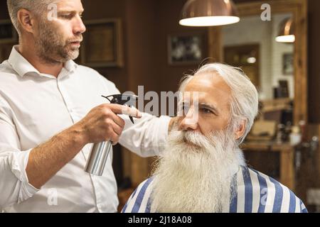 Coiffeur faisant une coupe de cheveux élégante pour un vieil homme beau Banque D'Images