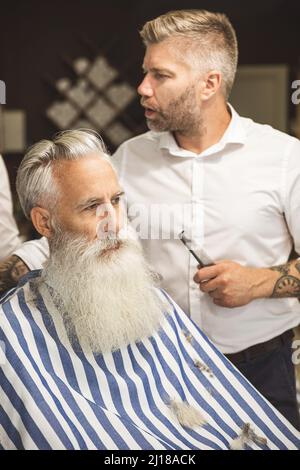 Coiffeur faisant une coupe de cheveux élégante pour un vieil homme beau Banque D'Images