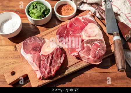 Deux steaks de bœuf cru, l'ossobuco, sur une planche de bois avec assaisonnement pour aromatiser les morceaux de viande. Concept de protéines animales, coupes de bœuf bon marché. Aereal vie Banque D'Images