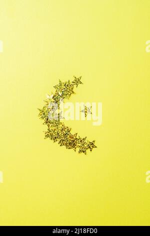 Forme de lune des paillettes luminescentes. Arrière-plan jaune et vue de dessus. Banque D'Images