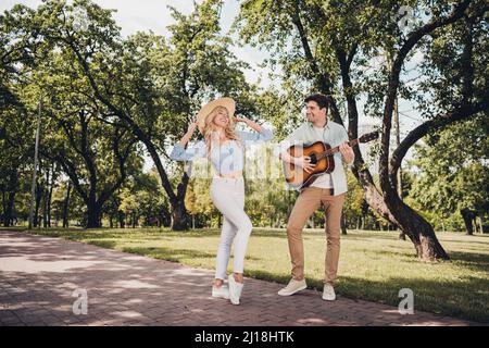 Vue sur toute la longueur du corps de deux beau heureux heureux couple gai jouant de la guitare danse avoir le repos amusant passe-temps sur l'air frais à l'extérieur Banque D'Images