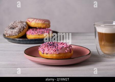 Beignets sur les assiettes et café avec mousse de lait dans une tasse résistante à la chaleur. Banque D'Images
