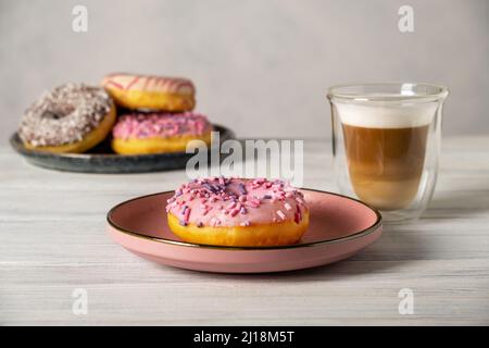 Beignets sur les assiettes et café avec mousse de lait dans une tasse résistante à la chaleur. Banque D'Images