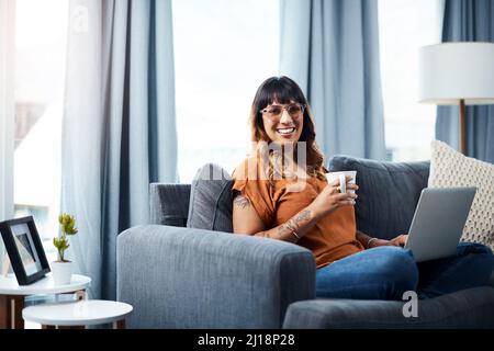 Aujourd'hui, je ne suis pas au fait de mes émissions préférées. Prise de vue d'une jeune femme utilisant son ordinateur portable tout en se relaxant à la maison. Banque D'Images