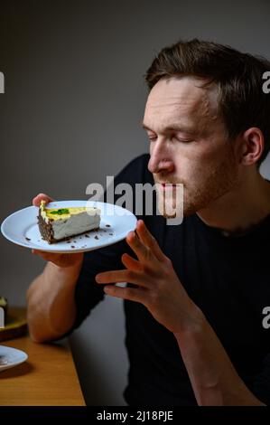 Un jeune homme tient une assiette de gâteau vegan dans sa main. Gâteau au cajou Banque D'Images