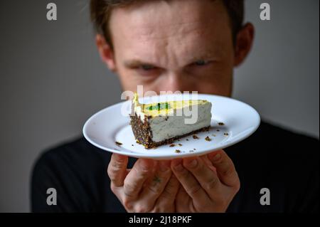 Un jeune homme tient une assiette de gâteau vegan dans sa main. Gâteau au cajou Banque D'Images