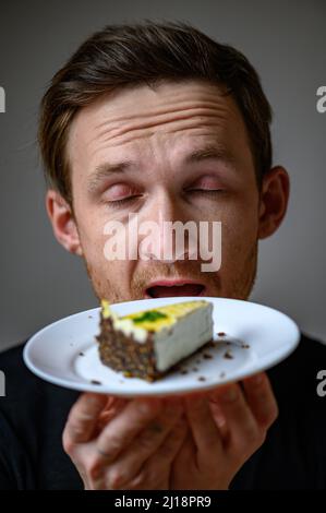 Un jeune homme tient une assiette de gâteau vegan dans sa main. Gâteau au cajou Banque D'Images