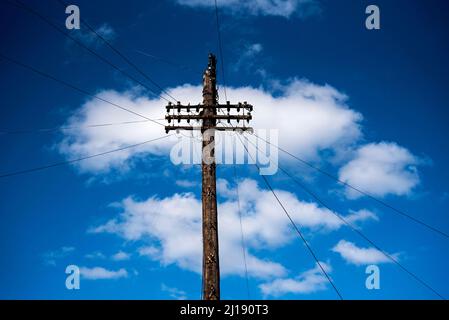 Poteau de télégraphe contre un ciel bleu avec des nuages blancs, les fils de téléphone s'éteignent dans toutes les directions. Banque D'Images