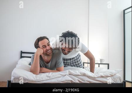 Couple gay heureux allongé sur la couette Banque D'Images