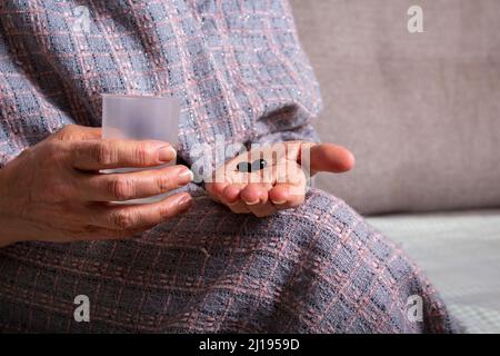 Vieille femme tenant dans la main des pilules noires. Banque D'Images