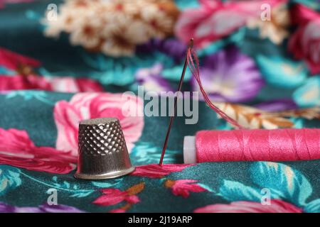 Filet avec aiguille et fil rose sur tissu satiné à motif fleuri vintage vert et rose Banque D'Images