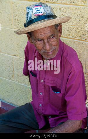 Un homme souriant regarde dans la rue à la Havane, Cuba, tout en portant un chapeau fedora avec une image vintage de Fidel Castro et le nom du président Jimmy carter. Banque D'Images