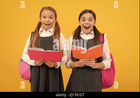 Surpris les enfants dans les uniformes formels lire les livres scolaires fond jaune, bibliothèque Banque D'Images