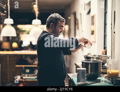 Juste un peu de sel. Prise de vue d'un chef spécialisé préparant un plat dans la cuisine d'un restaurant. Banque D'Images