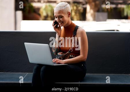 Messagerie instantanée : permet de regarder l'e-mail que vous avez envoyé en ce moment. Photo d'une jeune femme attirante utilisant son ordinateur portable tout en passant un appel téléphonique à l'extérieur. Banque D'Images