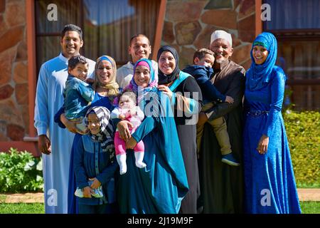 C'est une grande famille heureuse. Portrait d'une famille musulmane heureuse debout ensemble devant leur maison. Banque D'Images