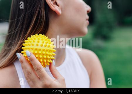 gros plan sur le visage de la jeune femme, orné d'une balle de massage piquée, pour une libération myofasciale et un soulagement de la douleur au niveau du cou et des épaules Banque D'Images