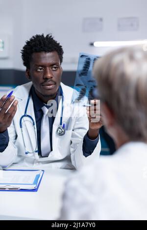 Un spécialiste en radiologie examine l'image d'acquisition en radiographie de la femme senior tout en expliquant le calendrier du traitement de récupération. Radiologue de la clinique discutant avec le patient malade du rapport de diagnostic. Banque D'Images