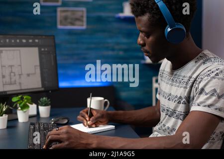 Architecte concepteur portant des écouteurs analysant des plans immobiliers concevant des prototypes de bâtiment travaillant à distance de la maison. Entrepreneur jeune adulte développant un produit architectural Banque D'Images