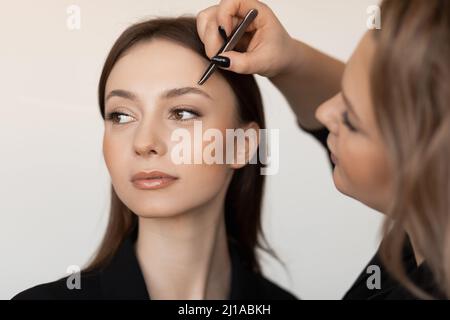 Gros plan d'une jeune femme impeccable avec de longs cheveux foncés qui ramèchent les sourcils d'un maquilleur professionnel vêtue de vêtements noirs. Banque D'Images