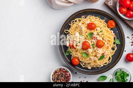 Pâtes cuites à la feta, aux tomates et à l'ail. Pâtes tendance à la feta aux herbes et au basilic sur fond gris. Vue de dessus, espace de copie. Banque D'Images