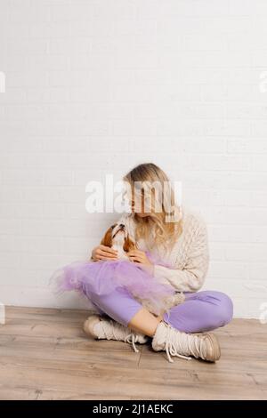 Une femme bien entretenue, tenue en chandail beige et pantalon violet, envoie des baisers au chien de spaniel dans le cape organza violet Banque D'Images