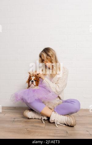 Belle femme en chandail beige, pantalon violet élever les oreilles de chien vers le haut spaniel portant violet organza cape avoir du plaisir. Banque D'Images