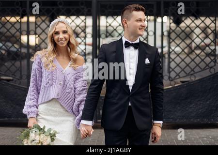 Jeune couple attrayant de mariée avec de longs cheveux ondulés équitables en robe, gilet lilas avec bandeau sur la tête et le marié. Banque D'Images