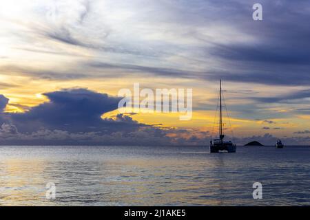 Coucher de soleil spectaculaire avec nuages de tempête à l'horizon, avec silhouette d'un yacht (catamaran) ancré dans la baie, Anse Lazio, île de Praslin, Seychelles. Banque D'Images