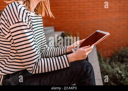 Jeune femme blonde souriante tenant une tablette, ayant des appels vidéo en ligne sur une tablette, e-learning, tutorat au travail dans la ville Banque D'Images