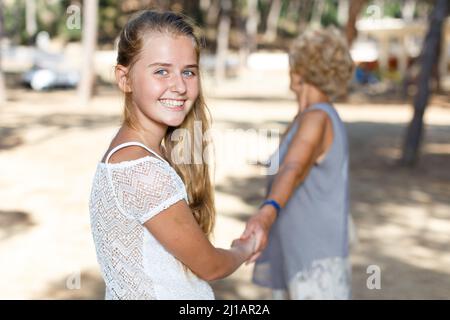 Vue arrière de l'adolescence jolie fille dans le parc vert tenir la grand-mère à portée de main Banque D'Images