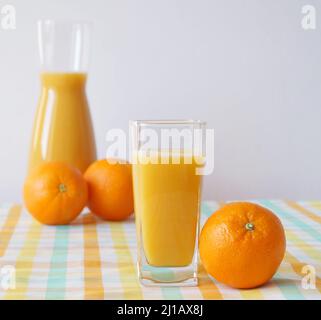 Un verre et une carafe de jus d'orange fraîchement pressés se tiennent sur une table avec une belle nappe, et des oranges fraîches sont à proximité - une charge d'ener Banque D'Images