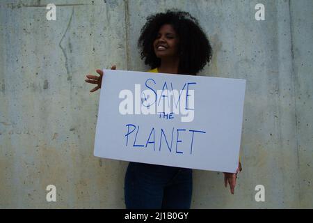 Une femme afro-américaine avec une bannière entre ses mains disant sauver la planète. Dans le mur gris d'arrière-plan Banque D'Images