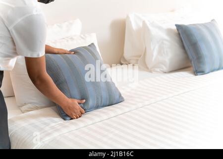 une femme de ménage vous met en place un oreiller sur un drap de lit dans la chambre d'hôtel Banque D'Images
