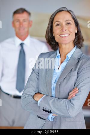 Confiant et réussi. Portrait d'une femme d'affaires mûre avec sa collègue debout à l'arrière-plan. Banque D'Images
