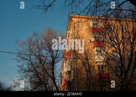 Immeuble d'appartements avec balcons rouges et gouttière éclairée par le soleil couchant. Branches d'arbres devant la maison au coucher du soleil d'hiver Banque D'Images