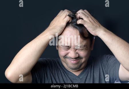 L'homme d'âge moyen a des démangeaisons dans ses cheveux sur fond noir, concept de soins de cheveux Banque D'Images