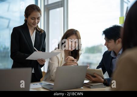 L'équipe de concepteurs de groupes de travail d'entreprise divers et le chef de file d'une femme asiatique discutent des données statistiques des rapports financiers de la paperasserie, en prévoyant des travaux communs Banque D'Images