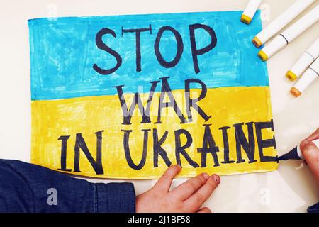 Petite fille ukrainienne dessine une image avec le drapeau de l'Ukraine et le texte ARRÊTER LA GUERRE EN UKRAINE. 2022 invasion russe de l'Ukraine. Banque D'Images