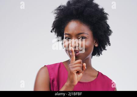 Je suis bien à garder des secrets. Portrait d'une jeune femme attrayante posant avec son doigt sur ses lèvres sur un fond gris. Banque D'Images
